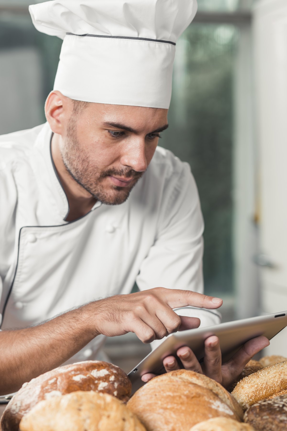 Cuisinier en toque saisissant un relevé sur tablette devant sa production du jour